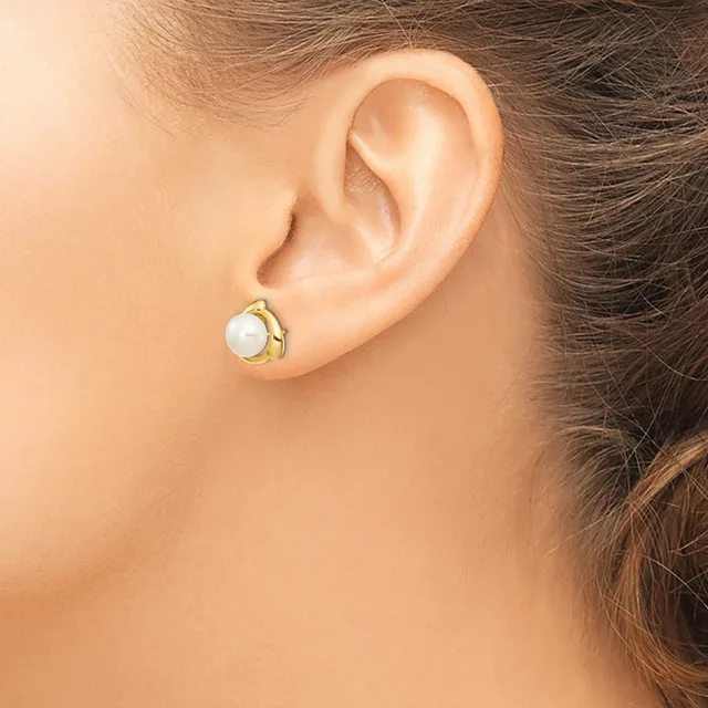 A person wearing a gold-toned stud earring with a white pearl set in a curved gold setting, shown from the side view of their ear.
