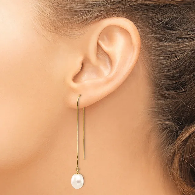 A person wearing a threader earring with a long delicate chain and a white pearl pendant hanging from the earlobe.
