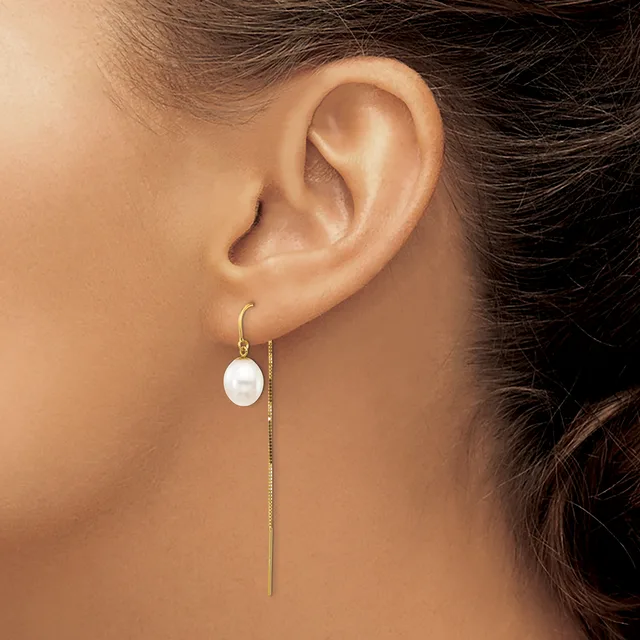 A person wearing a long threader earring with a white pearl drop on one end and a thin gold chain passing through the ear lobe.