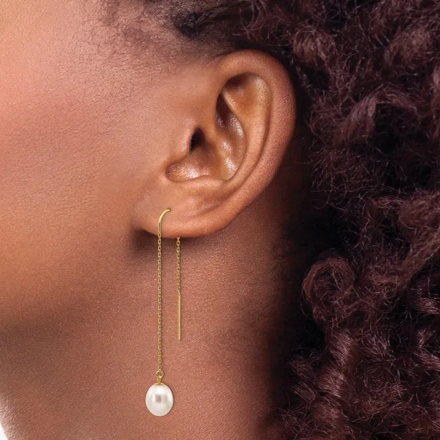 A person wearing gold threader earrings with pearl drops, shown from the side profile against their neck and shoulder.