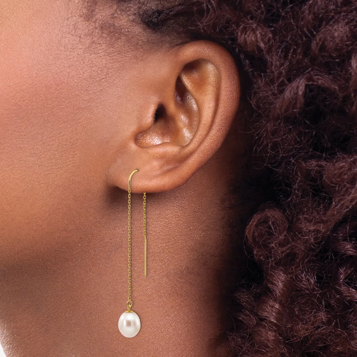 A person wearing gold threader earrings with pearl drops, shown from the side profile against their neck and shoulder.