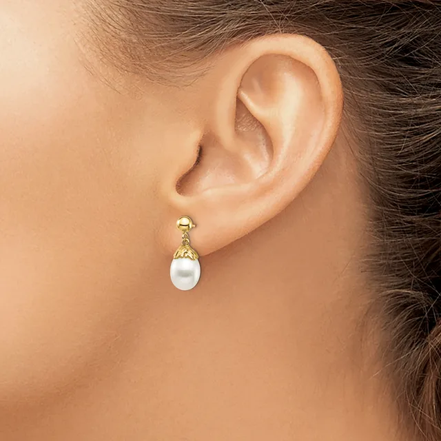 A person wearing a gold drop earring with a white pearl and textured gold cap, shown from the side view of their ear and neck.