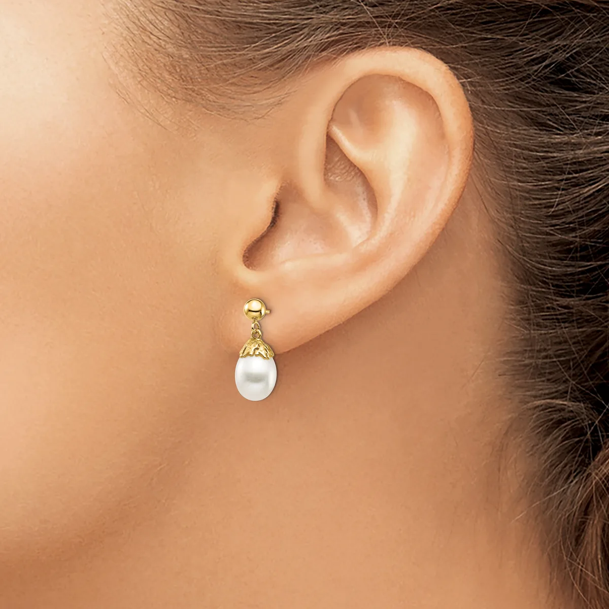 A person wearing a gold drop earring with a white pearl and textured gold cap, shown from the side view of their ear and neck.