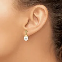 A person wearing a gold drop earring with a white pearl and textured gold cap, shown from the side view of their ear and neck.