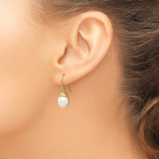 A person wearing a drop earring with a white oval stone set in a gold-toned metal cap and hook, shown on their ear from the side.