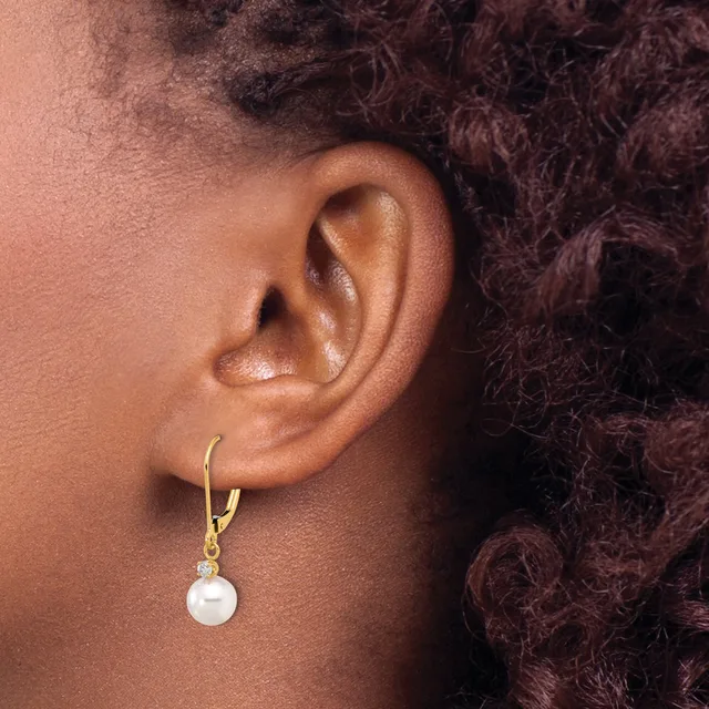 A person wearing a gold hoop earring with a white pearl pendant hanging from it, shown from the side against their ear and dark curly hair.