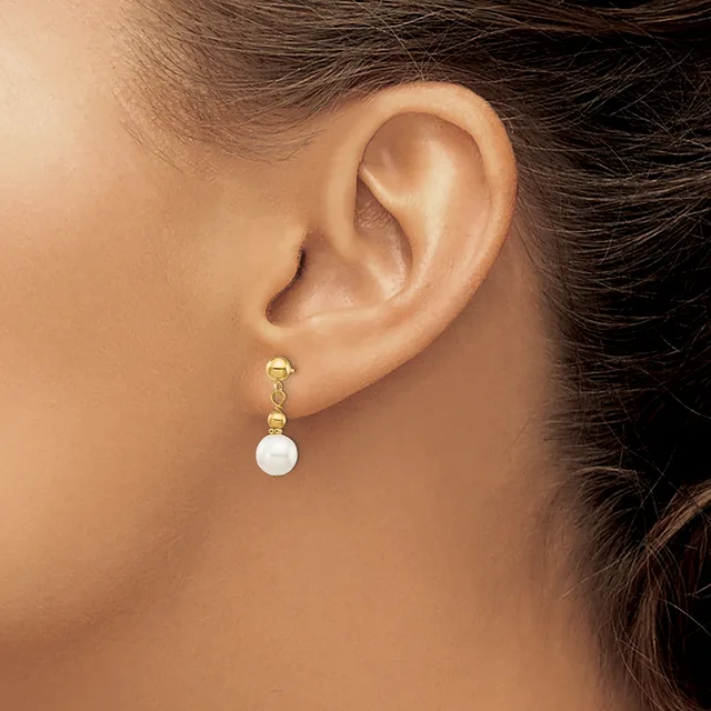 A woman wearing a gold dangle earring with small beads and a white pearl drop, shown from the side view of her ear and neck.