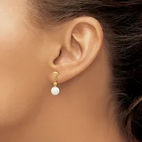 A woman wearing a gold dangle earring with small beads and a white pearl drop, shown from the side view of her ear and neck.