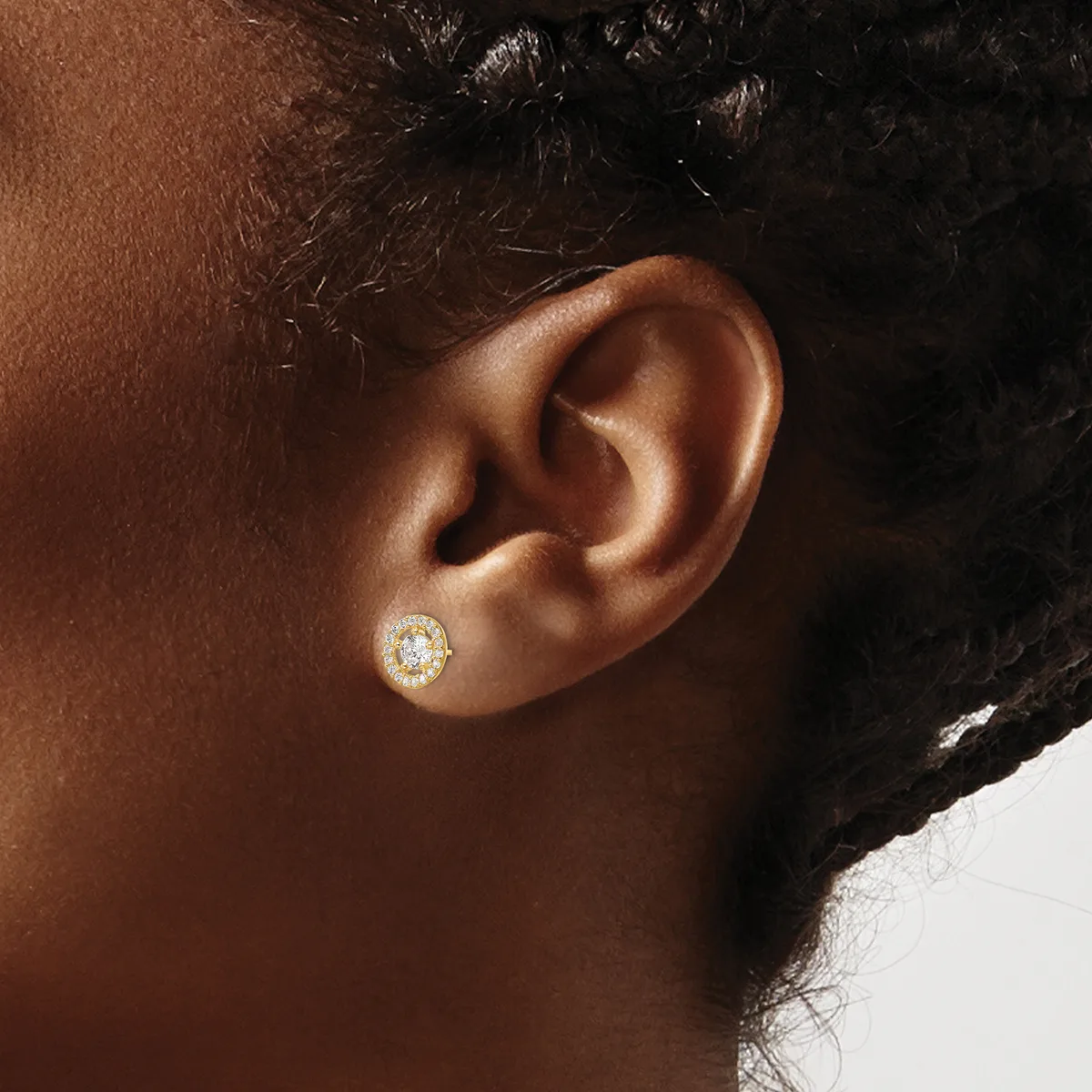 A person wearing a gold stud earring with a round diamond or crystal stone in the center of the lobe.