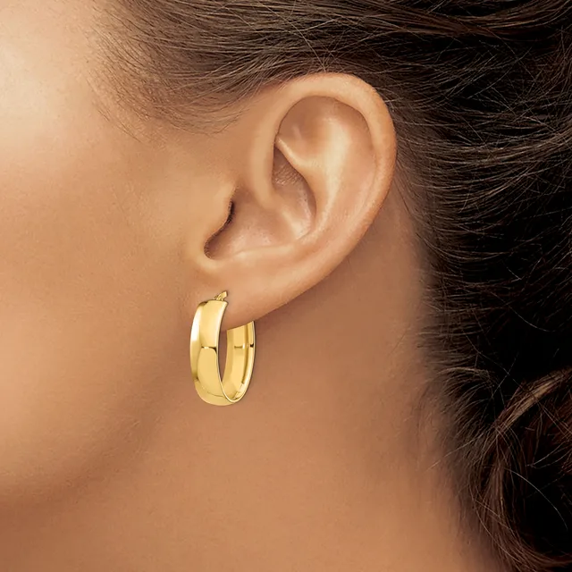 A person wearing a pair of polished gold hoop earrings with a chunky, curved profile, shown from the side view of their ear and neck.