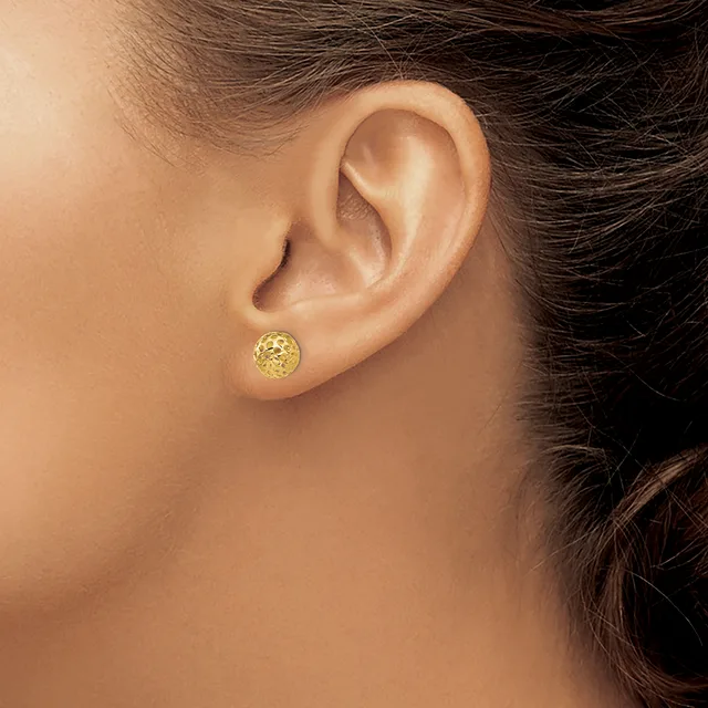 A person wearing a small round gold stud earring with a textured surface is shown in profile from the side of their face and ear.