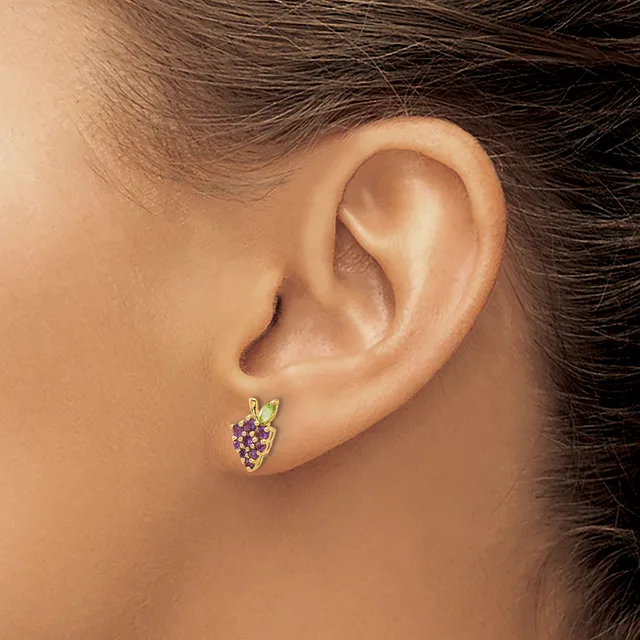 A person wearing a small gold stud earring set with purple gemstones in a shield or heart shape, shown from the side view of their ear.