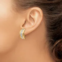 A gold and silver two-tone curved hoop earring with a textured surface worn on a person's earlobe.
