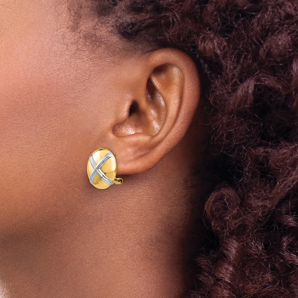 A person wearing a gold and silver crossover earring with a curved post, shown from the side view against their ear and neck.