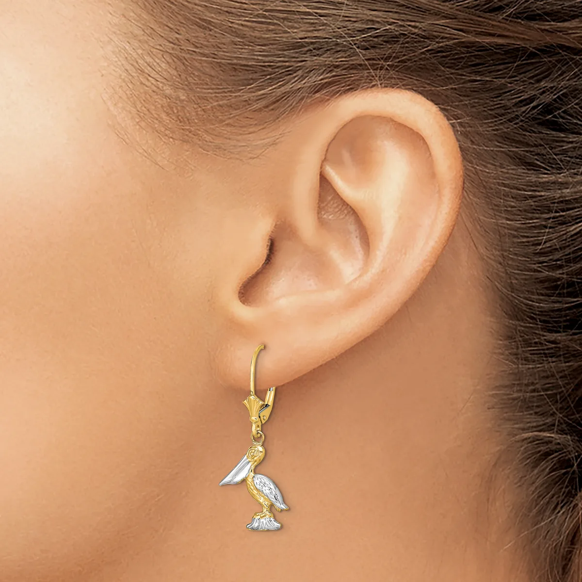 A person wearing a gold lever-back earring with a dangling two-tone bird charm featuring white enamel and diamond accents.