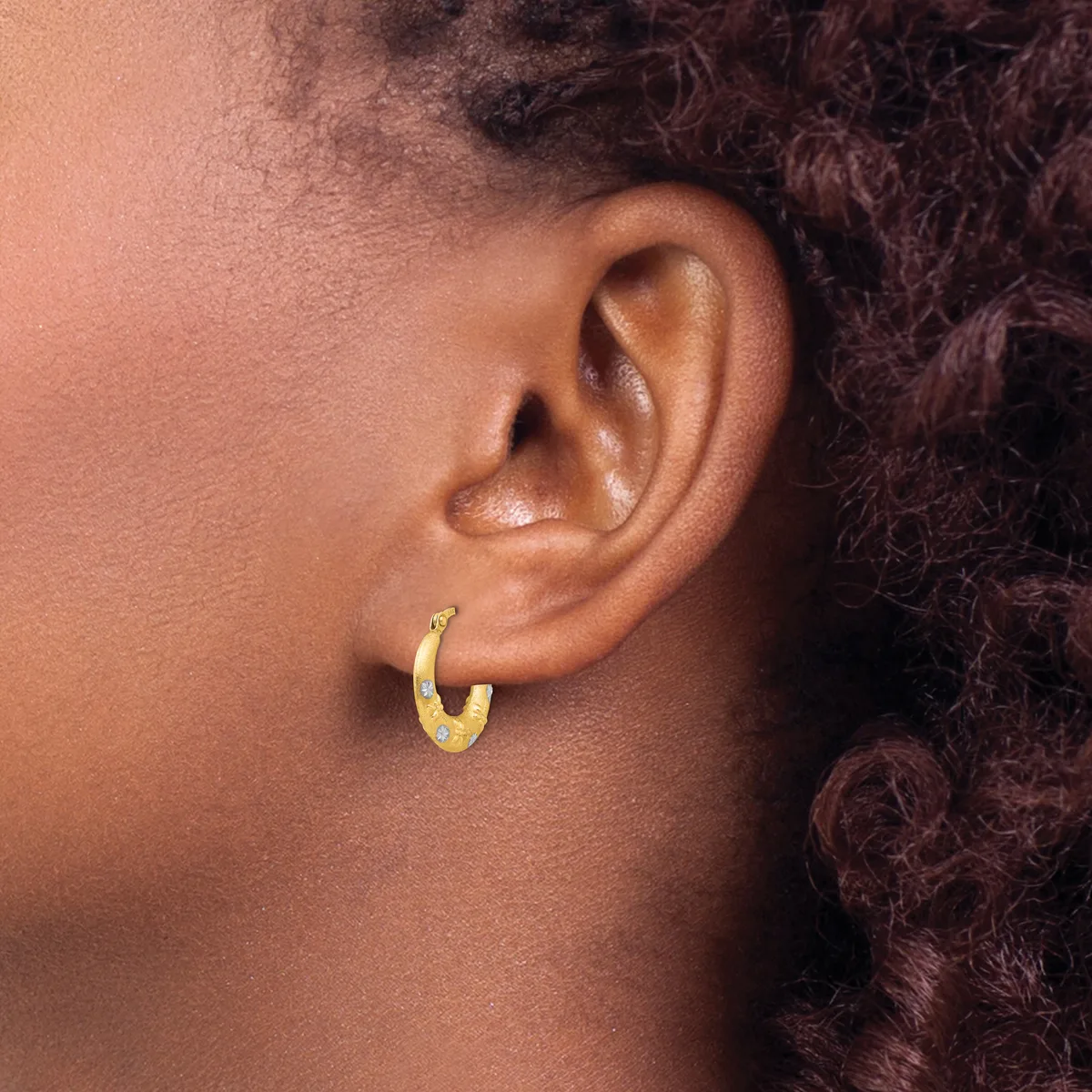 A person wearing a small gold hoop earring in their earlobe, shown in profile with dark curly hair visible.