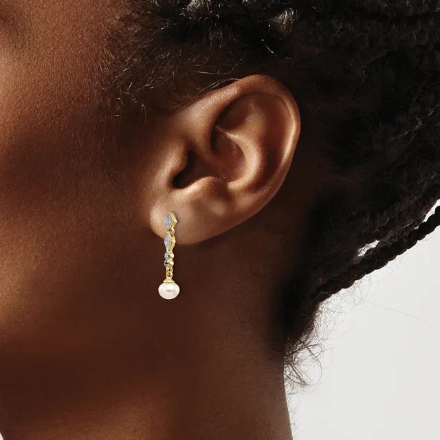 A person wearing a gold drop earring with a chain of small diamond-shaped stones and a white pearl at the end, shown from the side view.
