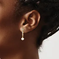 A person wearing a gold drop earring with a chain of small diamond-shaped stones and a white pearl at the end, shown from the side view.