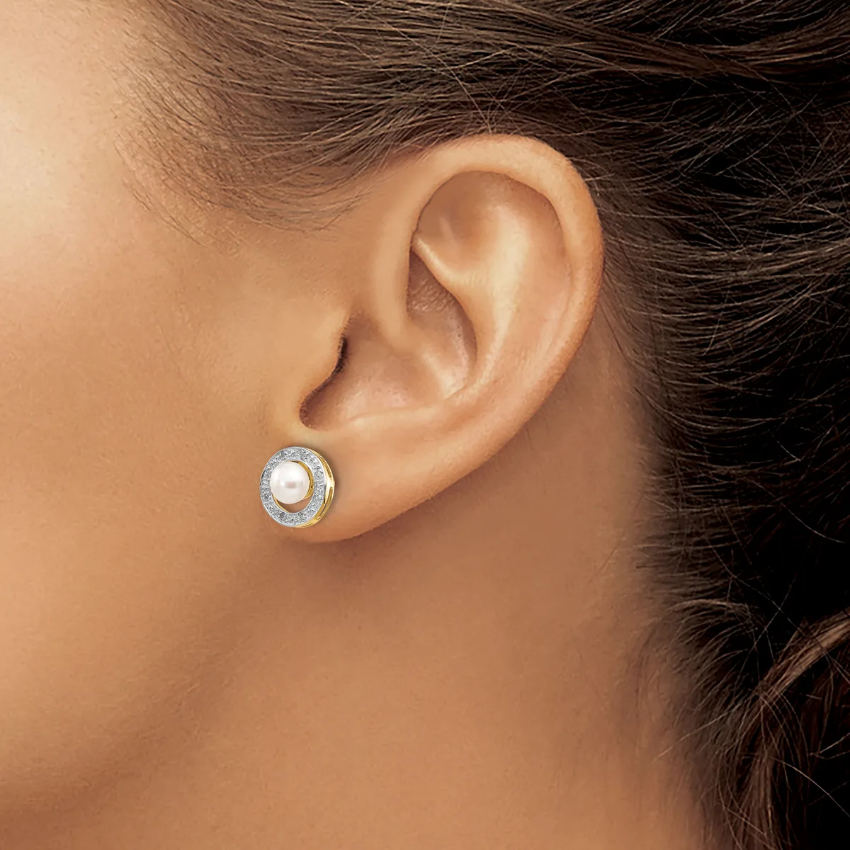A woman wearing a round stud earring with a white pearl center surrounded by small diamonds in a silver setting.