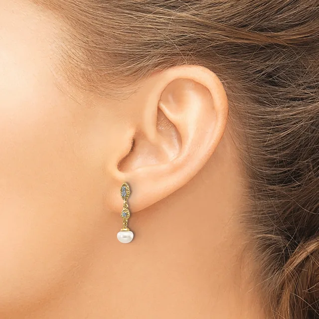A woman wearing a dangling earring with decorative diamond-shaped links at the top and a white pearl drop at the bottom.
