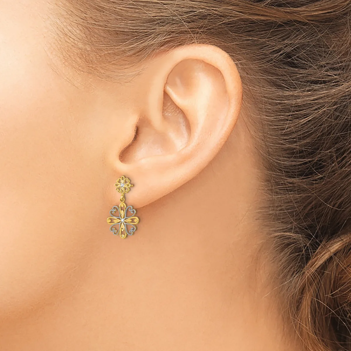A woman wearing a two-tier flower-shaped drop earring with yellow and white gemstones set in metal, shown from the side view of her ear and neck.