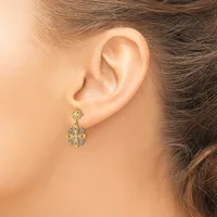 A woman wearing a two-tier flower-shaped drop earring with yellow and white gemstones set in metal, shown from the side view of her ear and neck.
