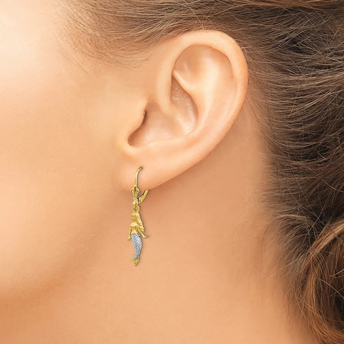 A person wearing a gold-toned drop earring with textured details and a small diamond or crystal accent, shown from the side view of their ear.