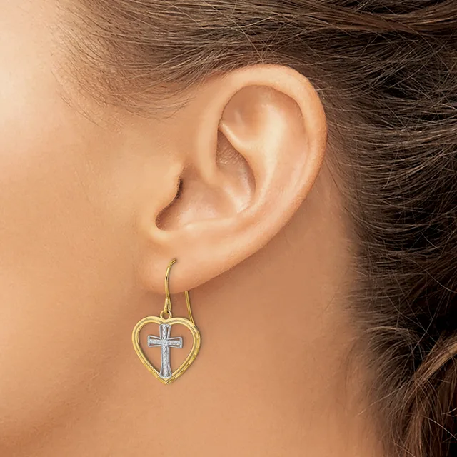 A woman wearing a heart-shaped earring with a cross design in the center, suspended from a curved hook, displayed against her ear.