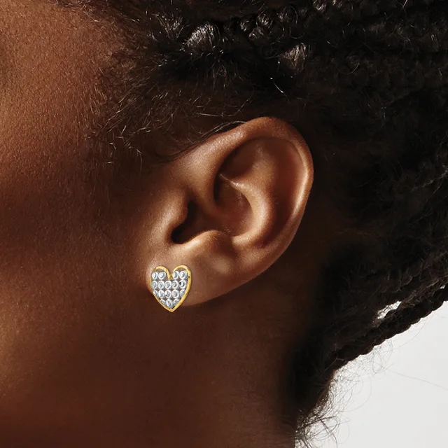 A heart-shaped silver stud earring set with small clear stones is worn in the earlobe of a person with medium skin tone and dark hair pulled back.
