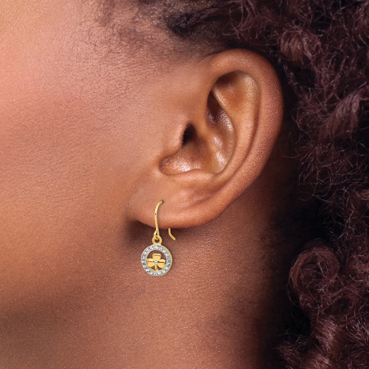 A person wearing a gold dangle earring with a round pendant featuring a citrine stone surrounded by small diamonds on a gold hook backing.
