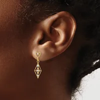 A gold drop earring with a heart-shaped post and a geometric diamond-shaped pendant hangs from a person's earlobe.