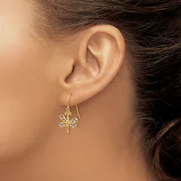 A person wearing gold drop earrings with a four-pointed star design set with small diamonds, shown from the side profile of their ear.