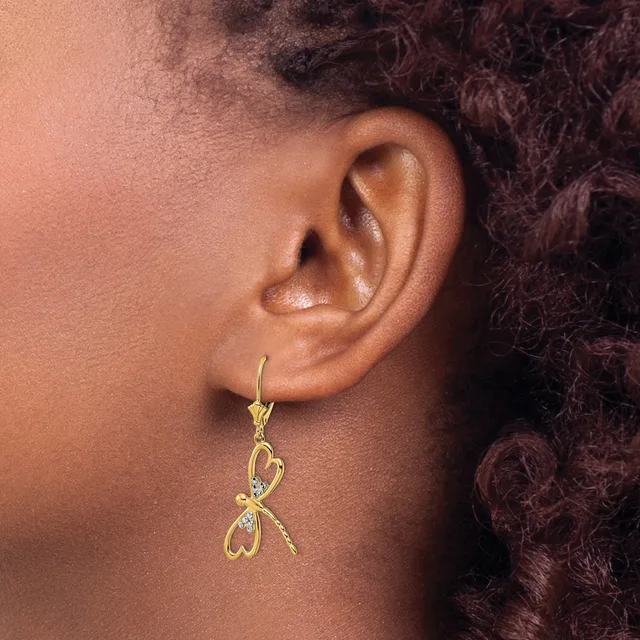 A gold dragonfly-shaped earring with rhinestone accents hangs from a lever-back ear wire on a person's earlobe.