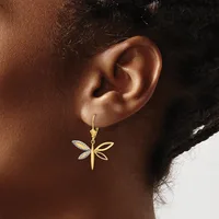 A gold dragonfly-shaped earring with diamond-set wings hangs from a gold ear wire on a person's earlobe.