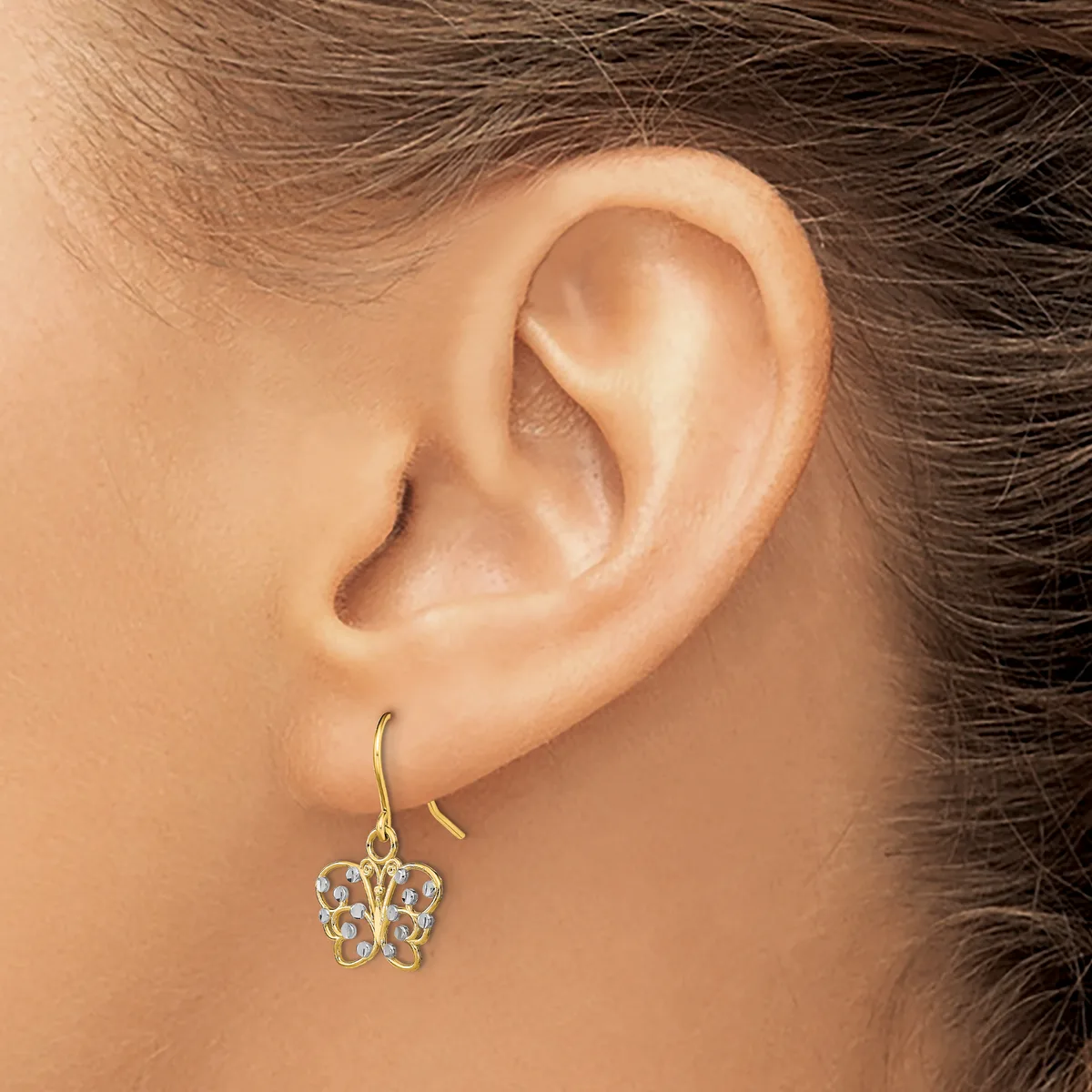A gold-toned butterfly-shaped earring with clear gemstones hangs from a curved hook on a person's earlobe.