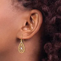 A person wearing a gold teardrop-shaped filigree earring with ornate scrollwork detail and a small center stone, shown from the side view against their ear.