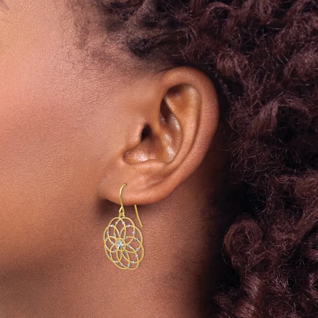 A person wearing a gold filigree teardrop-shaped dangle earring with an intricate circular floral pattern on a hook post.