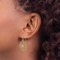 A person wearing a gold filigree teardrop-shaped dangle earring with an intricate circular floral pattern on a hook post.