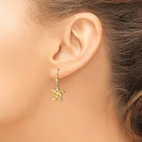 A gold turtle-shaped dangle earring hanging from a lever back hook worn on a person's earlobe.