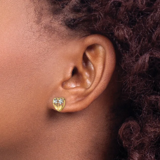 Close-up side view of a person's ear wearing a small gold heart-shaped stud earring with a clear gemstone center.