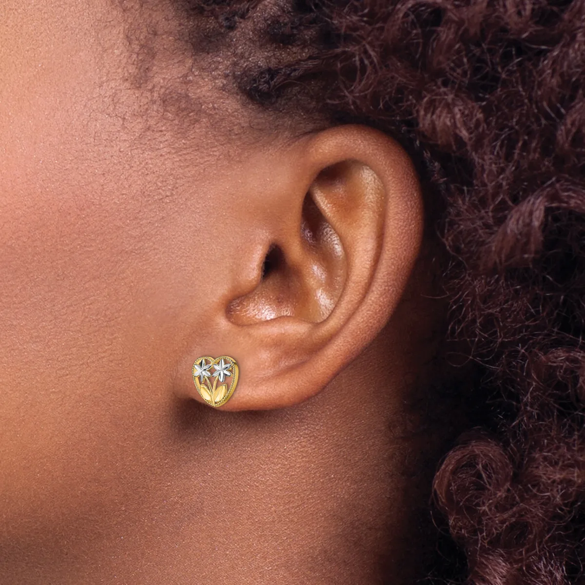 Close-up side view of a person's ear wearing a small gold heart-shaped stud earring with a clear gemstone center.