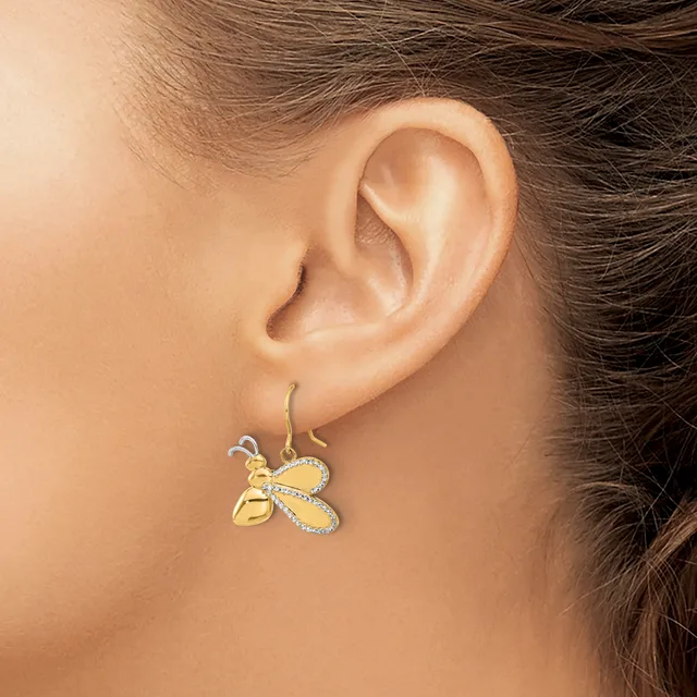 A woman wearing a gold bee-shaped earring with diamond accents on a hook wire, shown from the side view of her ear and face.