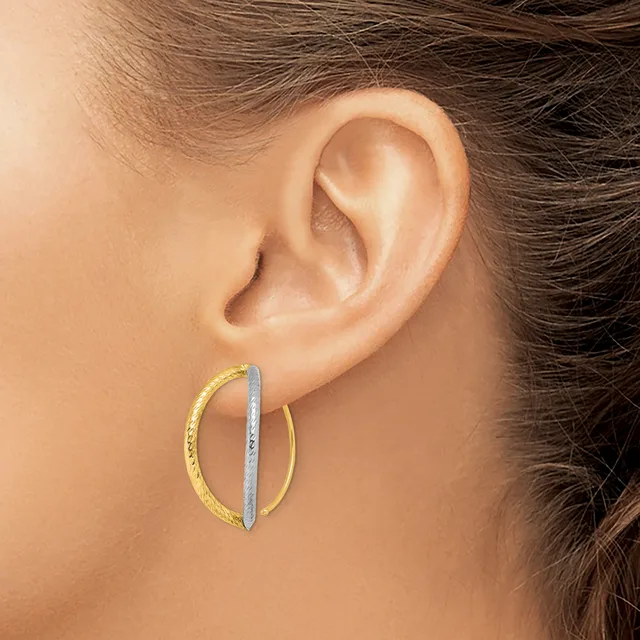 A person wearing two-toned hoop earrings with a textured gold outer hoop and a smooth silver inner hoop.