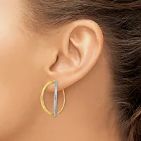 A person wearing two-toned hoop earrings with a textured gold outer hoop and a smooth silver inner hoop.
