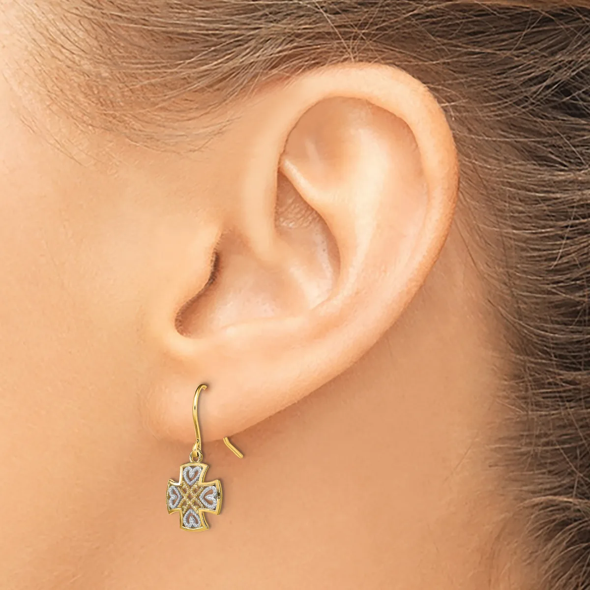 A woman wearing a four-leaf clover-shaped dangle earring with a textured silver and gold finish on a fish hook ear wire.