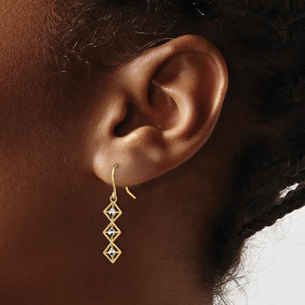 Gold drop earrings with three connected diamond-shaped geometric links hanging from wire hooks on a person's ear.