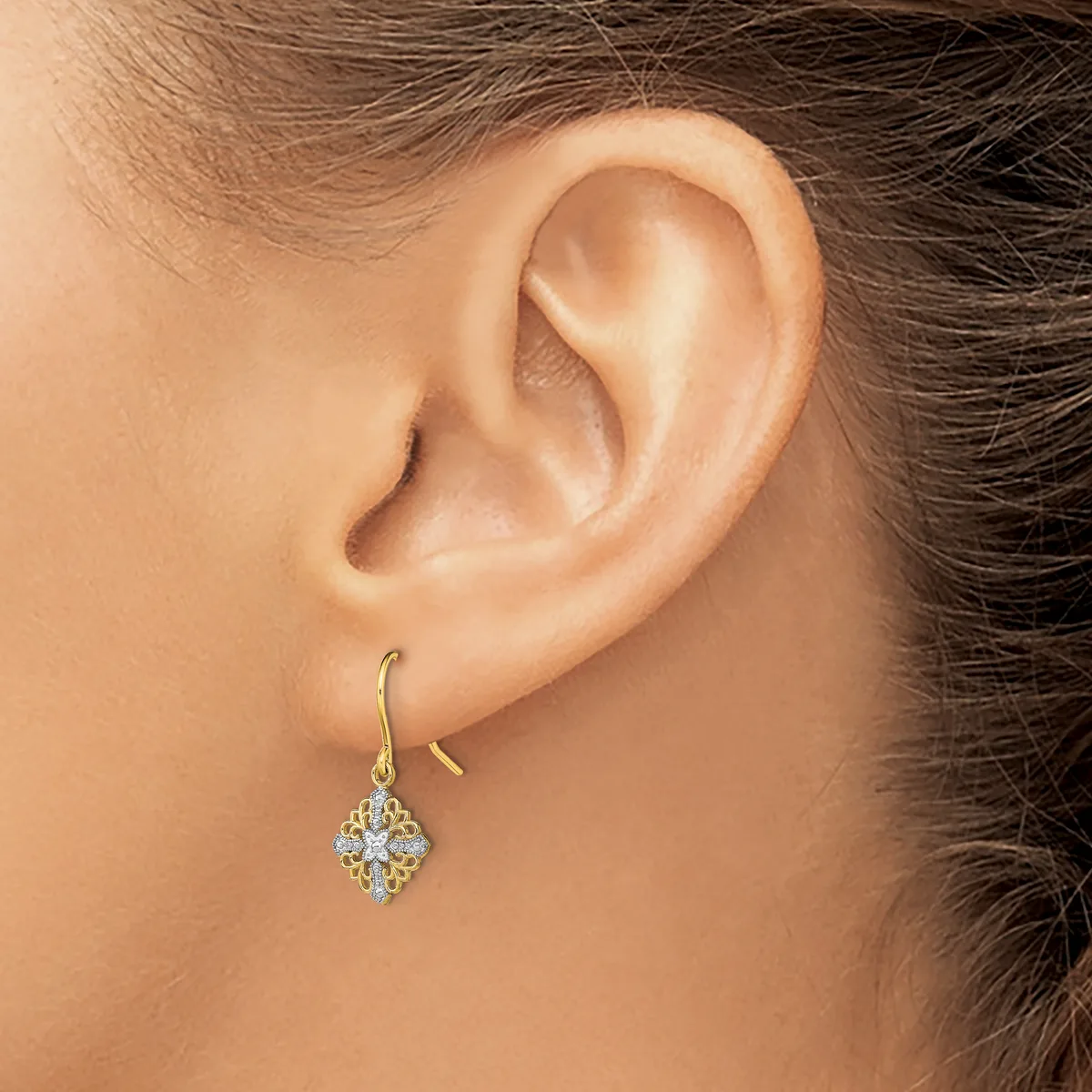 A woman wearing a gold hook earring with a diamond-shaped pendant composed of small sparkling stones hangs from her earlobe.