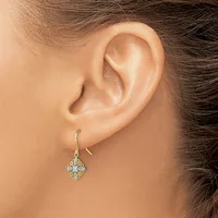 A woman wearing a gold hook earring with a diamond-shaped pendant composed of small sparkling stones hangs from her earlobe.