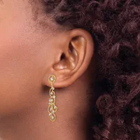 A woman wearing a long gold chain dangle earring with oval links and clear gemstones, shown from the side against her neck and shoulder with dark curly hair visible.