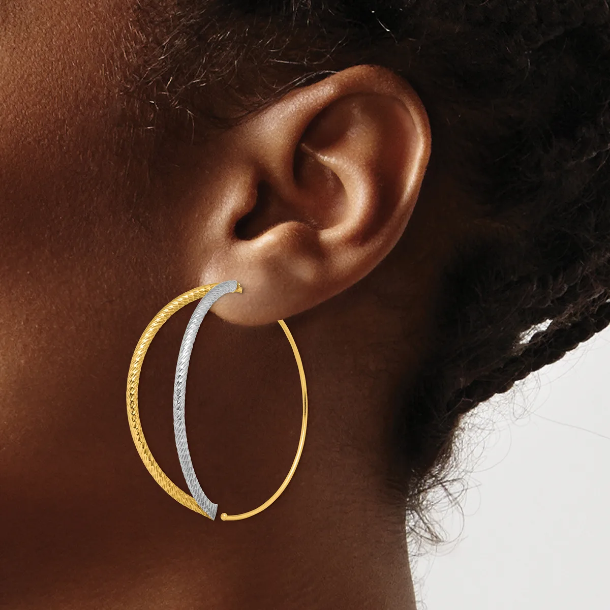 A person wearing two-tone hoop earrings with a gold outer band and silver inner band, shown from the side profile against a neutral background.